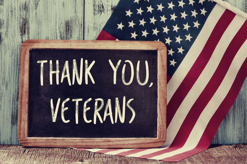 A blackboard in front of a white washed wall and an American Flag says, "Thank you, Veterans"