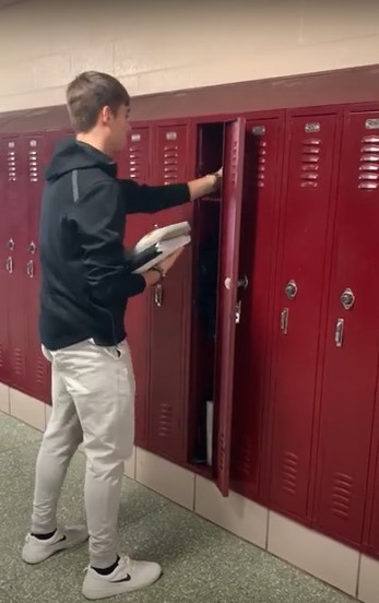A high school boy holding some books is reaching into a locker in a row of lockers
