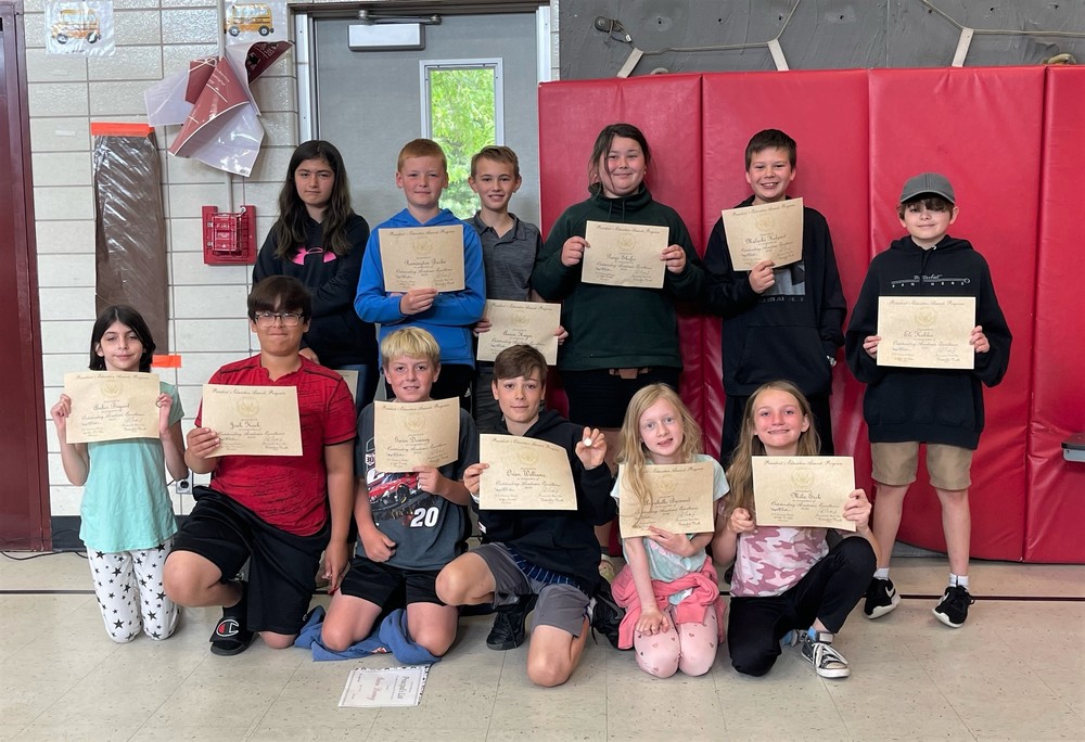 A group of 12 North School Students hold their President's Award for Educational Excellence certificates up in front of them to display.