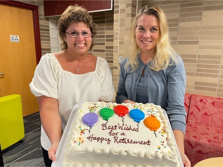 Sherry Cullitan and Heather Winter (two female teachers) are holding up a cake decorated with balloons and the words, "Best Wishes for a Happy Retirement