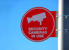 A round sign attached to a post.  The sign has a graphic of a security camera and the text, " security cameras in use".