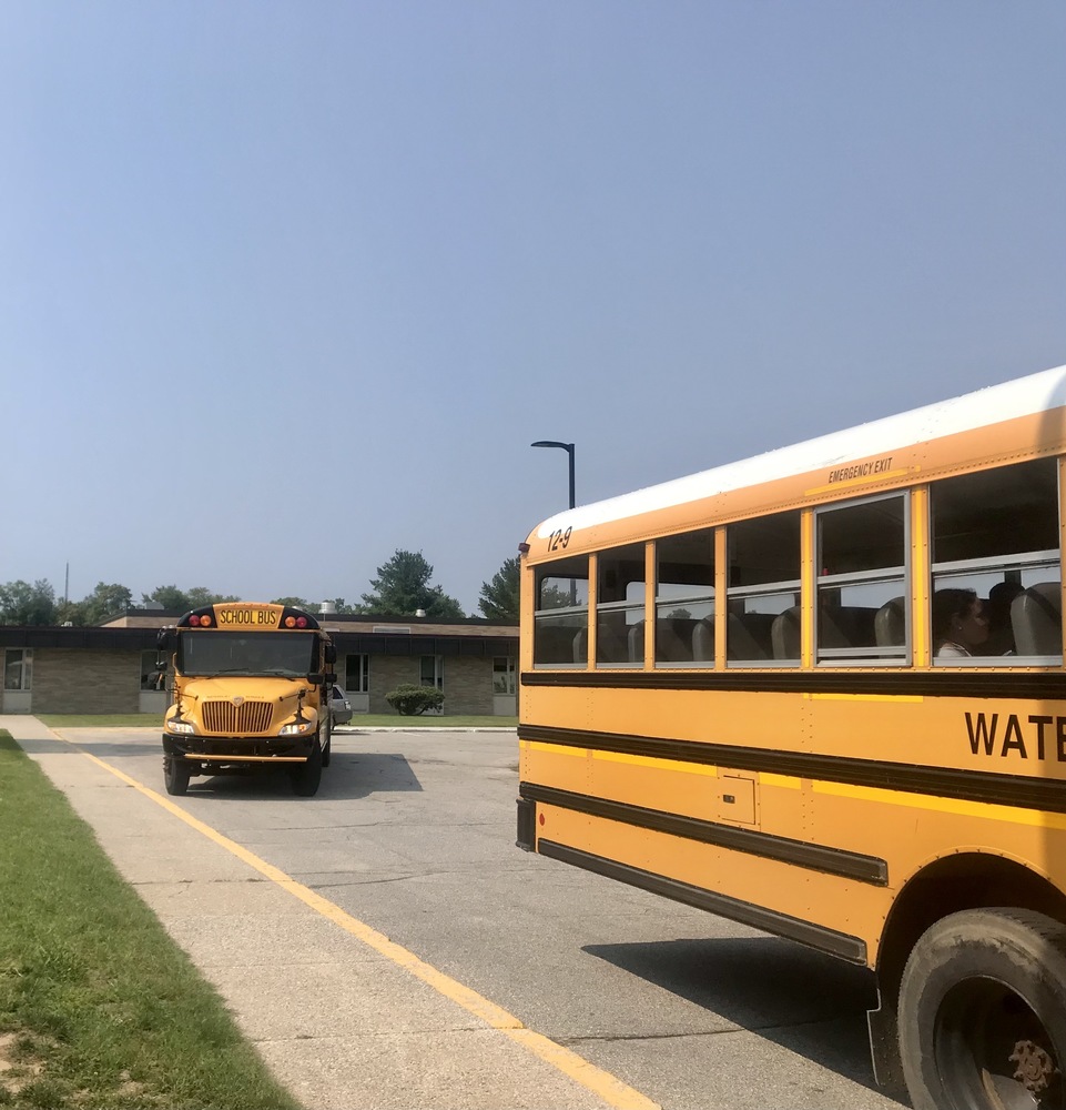 photo of the back half of a school bus in the foreground and the front of a school bus pulling up behind it in the background