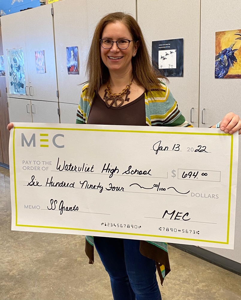 A smiling Marcella Hunt hold an oversized, mock check for $694.00  from MEC 