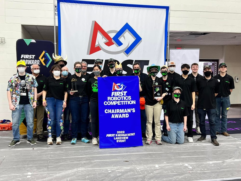 A group of individuals wearing face masks stands behind a sign reading," First Robotics Competition Chairman's Award, 2022 First in Michigan District Lakeview Event