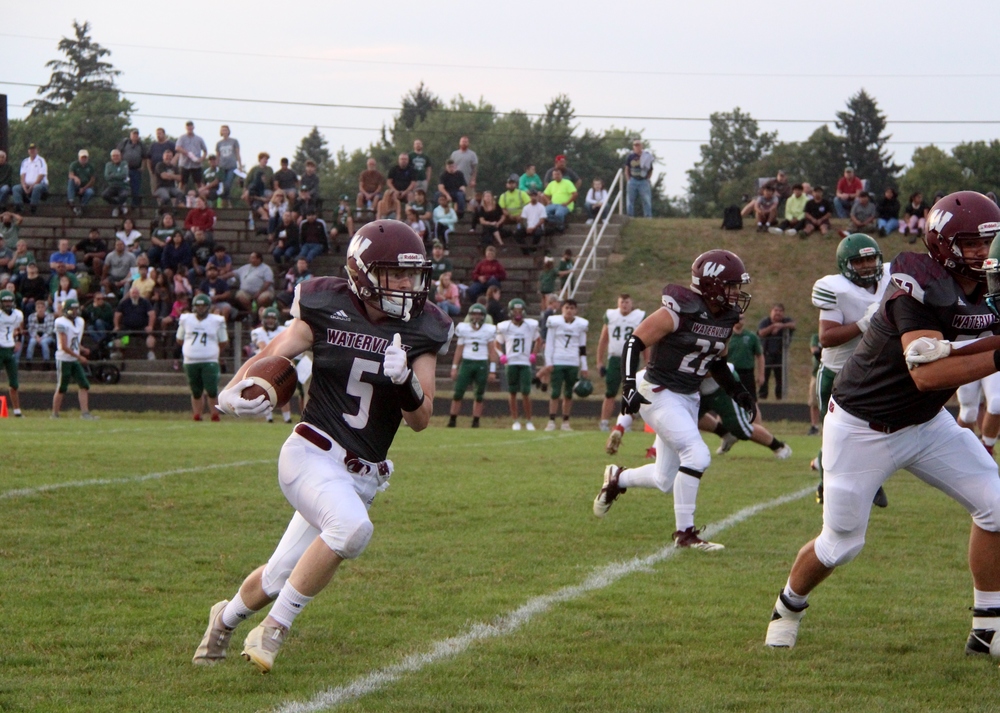 A Panther football player carries the ball in Panther Stadium running, presumably toward the goal.  Other Panther players can be seen in the photo, as well as the opponents on the sidelines and the visitors stands