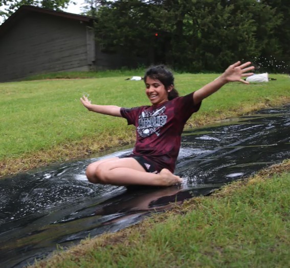 A girl of about 10 or 11 years is all smiles as she slides down a slip-n-slide style water slide.