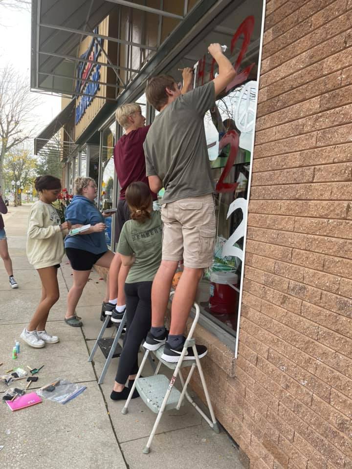 High School Students painting a downtown storefront window for Homecoming
