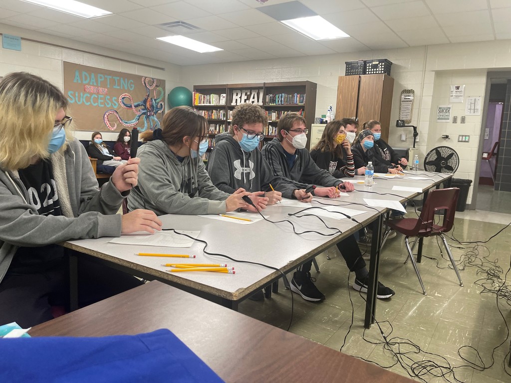 Several Quiz bowl contestants are seated at a table holding corded buzzers to use as they participate in the  competition