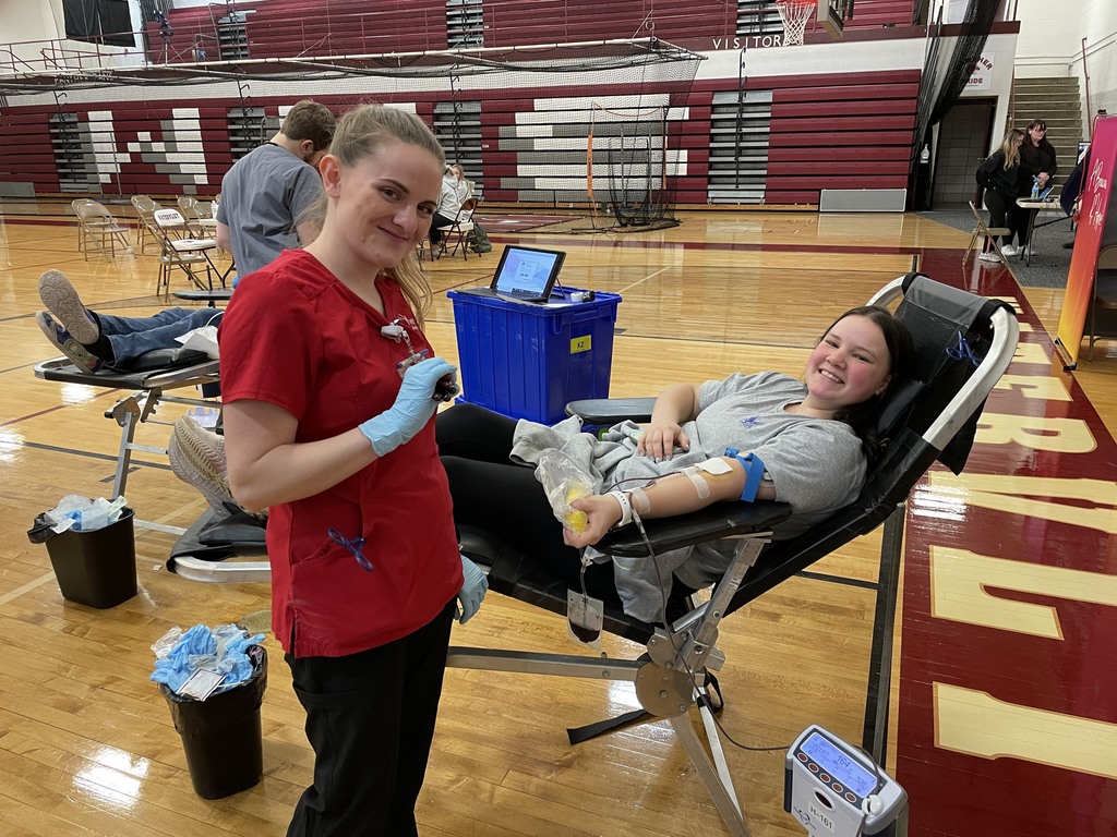 a phlebotomist smiles in front of a high school girl who is giving blood 
