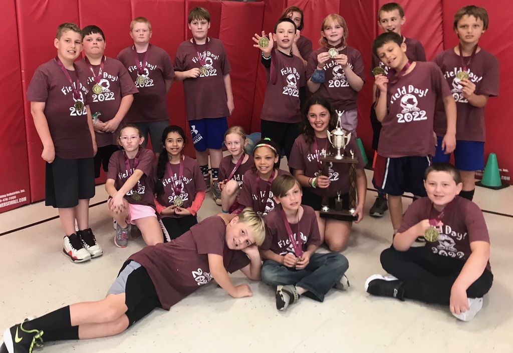 A group of about 20 5th grade students all wearing maroon Field Day! 2022 T-shirts are waring medals on ribbons around their necks that they won for sportsmanship at field day.