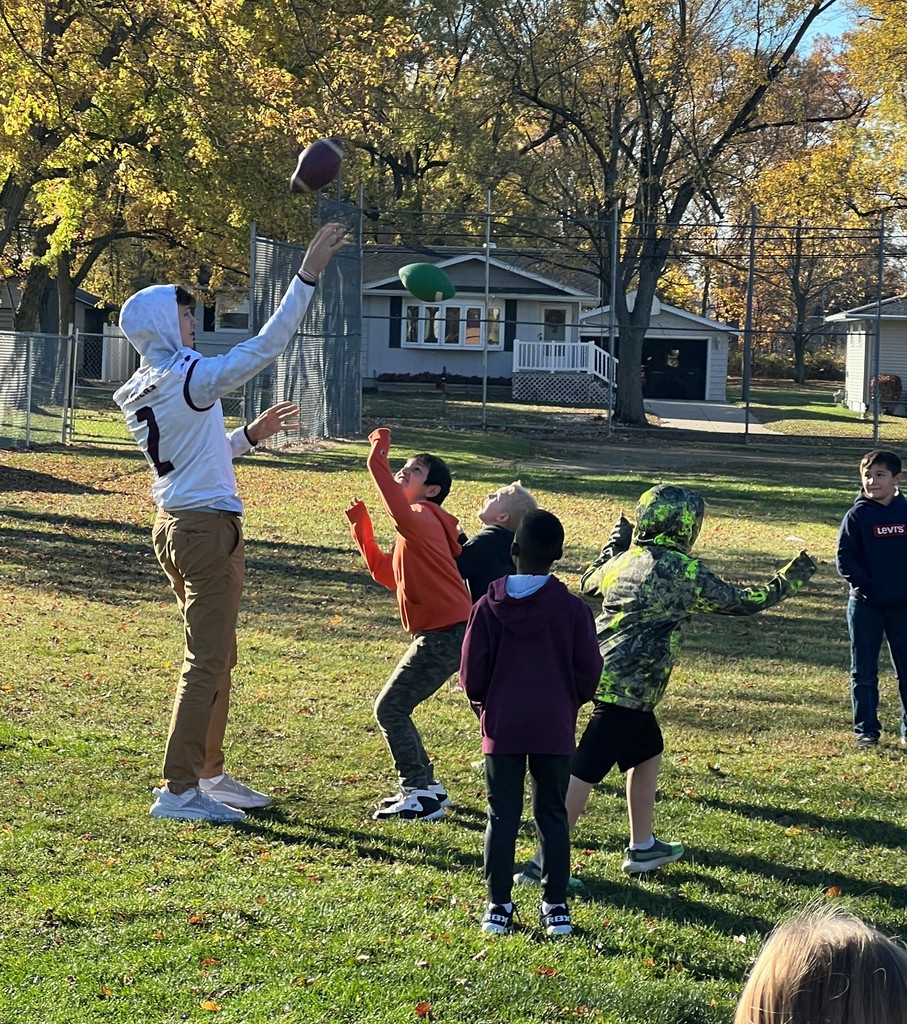 some elementary age boys and a high school age boy wearing a Panther football jersey are playing with footballs outdoors