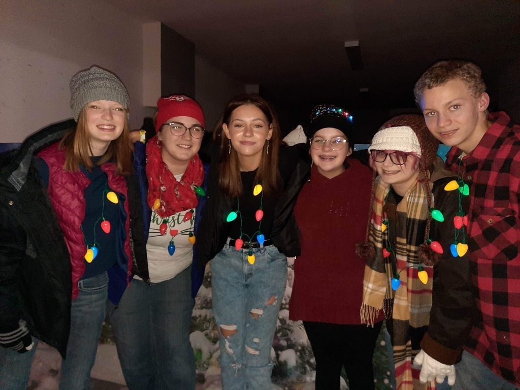 Five girls and one boy, high school age, wearing coats and hats, and lighted Christmas bulb necklaces