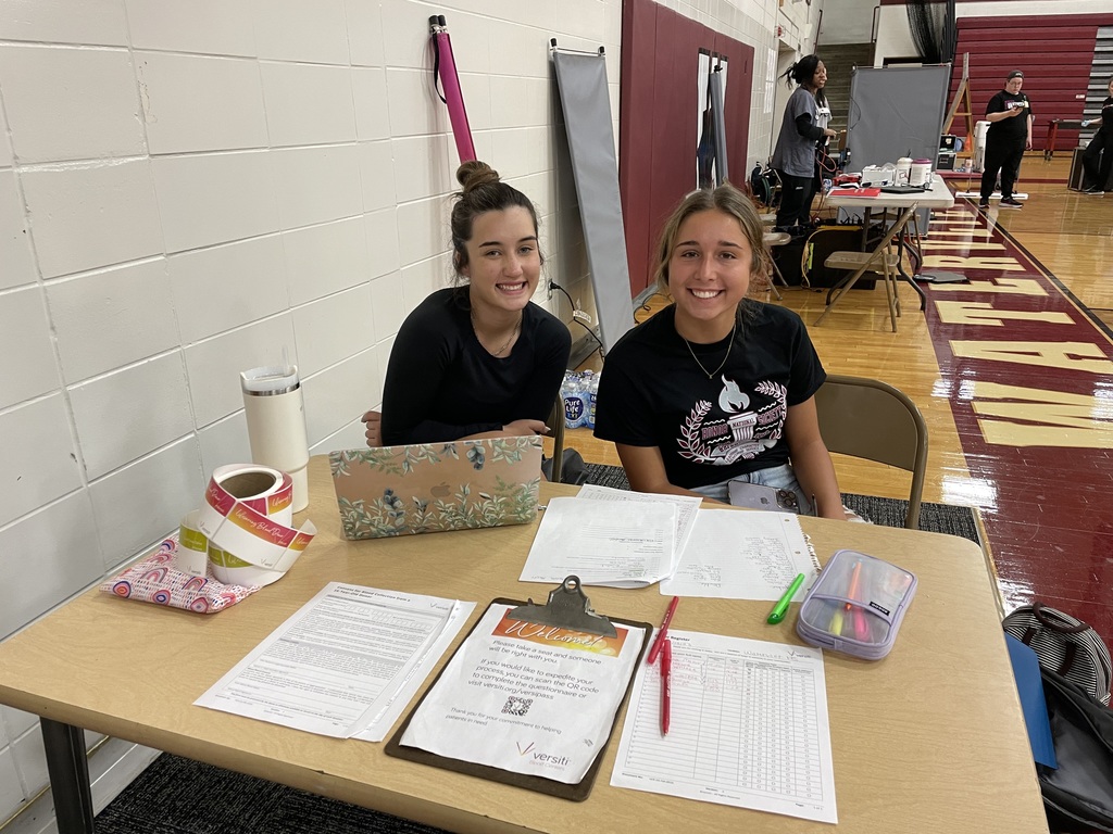 two girls sitting behind a table with papers, clipboard, and pens
