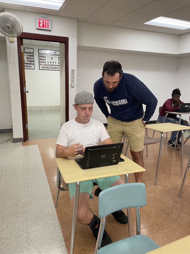 teacher looking over students shoulder at computer work
