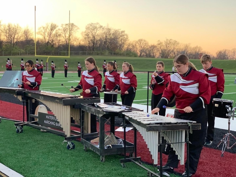Members of the band percussion section in full uniform playing their instruments on the football field